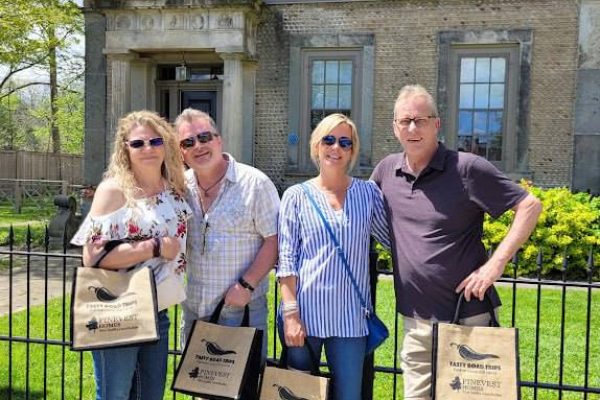 two couples taking a photo with tasty road trips handbags in front of a house